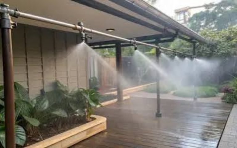 Mist Cooling System dealer setup with misting nozzles spraying a fine water mist over a wooden outdoor deck and plants.